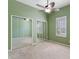 This bedroom features mirrored closet doors, green walls, neutral carpet, and a ceiling fan with a light at 3608 Mount Hope Loop, Leesburg, FL 34748