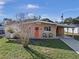 Tan mid-century modern home with orange door, landscaped lawn, and long driveway at 1514 Doreen Ave, Ocoee, FL 34761
