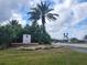 Entrance to The Palms Club featuring lush landscaping and a prominent sign under a sunny, cloudy sky at 5518 Metrowest Blvd # 104, Orlando, FL 32811