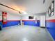 View of the epoxy-floor finished garage with painted blue and red accent walls, plus a wall mounted TV at 651 Tortugas St, Haines City, FL 33844