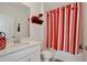 Bright bathroom with white vanity, quartz countertop, and shower with a red and white striped curtain at 2429 Volunteer Ave, Kissimmee, FL 34744