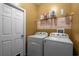 Functional laundry room with white washer and dryer, shelf with supplies and a white door at 13713 Meadowpark Ave, Orlando, FL 32826