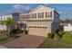 Two-story home featuring tan siding, red shutters, a brick driveway and an attached two-car garage at 613 Bloom Ter, Davenport, FL 33837