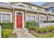 Charming townhome entrance featuring a vibrant red door, lush landscaping, and a white picket fence at 2602 Lodi Cir # 105, Kissimmee, FL 34746