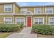 Attractive townhouse featuring a bold red door framed by manicured bushes and well-maintained surroundings at 2611 Gala N Rd # 105, Kissimmee, FL 34746