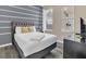 Cozy bedroom with grey and white striped accent wall, plush bedding, and a view to the outside at 2621 Archfeld Blvd, Kissimmee, FL 34747