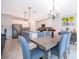 Modern dining room featuring an elegant chandelier, a wooden table and blue upholstered chairs, and kitchen views at 4418 Blackbird St, Kissimmee, FL 34746