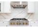 Close up of range with a stainless steel range hood, marble backsplash, and white cabinets with gold hardware at 10055 Brocksport Cir, Gotha, FL 34734