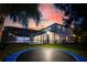 Expansive backyard at twilight, featuring a trampoline and a beautifully lit home with a screened-in pool area at 1910 Lake Roberts Landing Dr, Winter Garden, FL 34787