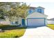 Two-story home with a tree in the yard, a two-car garage, and a blue front door at 608 Bluebill Ct, Kissimmee, FL 34759