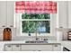 Bright kitchen sink with white cabinetry, red and white checkered window valances and view of the backyard at 340 W 9Th Ave, Mount Dora, FL 32757