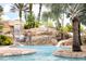 Tropical lagoon-style pool with a rocky waterfall feature, surrounded by palm trees and lush vegetation at 314 Muirfield Loop, Reunion, FL 34747