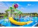 View of the splash pad with a blue safety surface, colorful equipment, and a pond with a fountain in the distance at 7671 Otterspool St, Kissimmee, FL 34747