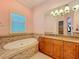 Main bathroom featuring a soaking tub, tiled surround, light wood cabinets, granite countertop, and a bright window at 1502 Hempel Ave, Windermere, FL 34786