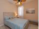 Comfortable bedroom with light-colored wood-look floors, bench, ceiling fan, and a beach scene wall print at 8011 Saint James Way, Mount Dora, FL 32757