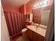 Well-lit bathroom featuring a vanity with a sink, toilet, and shower with a red curtain at 2450 Southern Oak St, The Villages, FL 32162