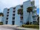 Exterior view of a blue condo building with multiple floors, balconies, tropical trees, and parking spaces at 4153 S Atlantic Ave # 1070, New Smyrna Beach, FL 32169