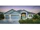 Charming one-story home boasts a three-car garage and inviting light-blue front door, set against a twilight sky at 6148 Gracie Pl, Lakeland, FL 33812