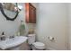 This half bathroom features a pedestal sink, round mirror, and wood storage cabinet above the toilet at 10384 Se 41St Ter, Belleview, FL 34420