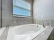 A close-up of a soaking tub featuring neutral tile surround and a window with blinds at 917 Carmillion Ct, Groveland, FL 34736