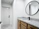 Bathroom featuring a wood vanity, granite countertop, round mirror, and door to the shower at 10012 Silver Bluff Dr, Leesburg, FL 34788