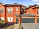 Townhouse featuring an attached garage, gray roof, and vibrant orange exterior paint at 142 Villa Di Este Ter # 204, Lake Mary, FL 32746
