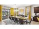 Dining area with a long wooden table set for a meal, complemented by yellow curtains and access to an outdoor patio at 7845 Oak Reflection Loop, Davenport, FL 33837