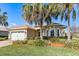 Inviting single-story house featuring lush landscaping, including palm trees, and a brick driveway leading to an attached garage at 10144 Lake Miona Way, Oxford, FL 34484