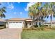 Charming single-story home showcasing a well-manicured lawn, palm trees, and a brick driveway leading to a two-car garage at 10144 Lake Miona Way, Oxford, FL 34484