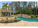 Tropical pool area with a rock waterfall feature, lush landscaping, and a covered outdoor dining area at 11324 Bridge House Rd, Windermere, FL 34786