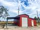 A vibrant red outbuilding with a roll-up door and sheltered area, ideal for projects or equipment storage at 111 Water Tank Rd, Haines City, FL 33844