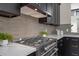 Close up on stove cooktop with grey backsplash and marble counters, enhanced by black cabinets and hardware at 13631 Guildhall Cir, Orlando, FL 32828