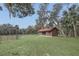 Property showcasing a spacious lawn, fenced area, and cozy home with a striking red roof amidst mature trees at 255 Butterfly Forest Rd, Geneva, FL 32732