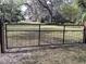 A black metal gate with a mesh design is set between wooden posts in a grassy yard at 1780 Old Mission Rd, Edgewater, FL 32132