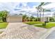 Paver driveway leading to a tan home with a well-maintained lawn and tropical landscaping at 2439 Teton Stone Run, Orlando, FL 32828
