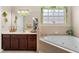 Bright bathroom features a soaking tub with tiled surround, dual vanity, and a plant over the window at 302 Vista Loop, Davenport, FL 33897