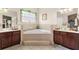 Bright bathroom features a soaking tub with tiled surround between dual vanities and a window with decorative plant at 302 Vista Loop, Davenport, FL 33897