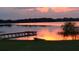 Scenic lake view at sunset with a dock and a small boat resting on the grassy bank at 9130 Laws Rd, Clermont, FL 34714