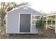 Exterior view of the shed, with a grey finish, complemented by a window and mature landscaping at 9130 Laws Rd, Clermont, FL 34714