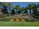 Community entrance featuring a stone sign, manicured landscaping, and swaying palm trees at 938 Braewood Dr, Clermont, FL 34715