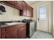 This laundry room features wood cabinets, gray countertops, a stainless steel washer and dryer, and stylish tile flooring at 1220 Lake Mills Rd, Chuluota, FL 32766