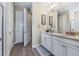 Well-lit bathroom featuring double sinks, a granite countertop, wood-look flooring, and doors to the shower and hallway at 211 Venetian Palms Blvd, New Smyrna Beach, FL 32168