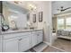 Bathroom with double sinks, granite countertop, wood-look flooring, and an open doorway to the Primary bedroom at 211 Venetian Palms Blvd, New Smyrna Beach, FL 32168