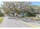 Street view of a charming blue house shaded by large oak trees, set back from the road with a fenced yard at 9350 2Nd Ave, Orlando, FL 32824