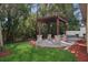 Backyard featuring a paved patio with a wooden pergola supported by stone columns, surrounded by mulch and grass at 981 Galway Blvd, Apopka, FL 32703