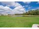 Scenic backyard view of a lush lawn, serene pond, and townhome exteriors under a bright, partly cloudy sky at 14849 Driftwater Dr, Winter Garden, FL 34787