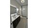 Modern bathroom with large illuminated mirror, dark vanity, and shower featuring a pebble floor at 36104 Emeralda Ave, Leesburg, FL 34788