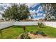 Large backyard featuring green grass, tropical trees and plants, rock beds and a tall white fence at 730 Garberia Dr, Davenport, FL 33837