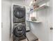 Compact laundry area with stacked washer and dryer, complemented by open shelving for storage at 12100 Calaboose Ct, Orlando, FL 32828