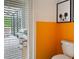 Bright bathroom featuring a toilet, orange accent wall, Mickey Mouse art, and a view of the patio through the shuttered door at 2904 Penelope Loop, Kissimmee, FL 34746